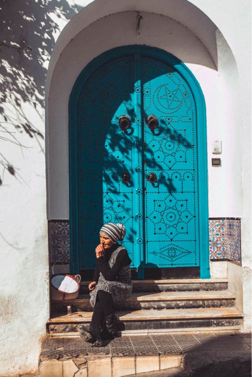 Femme assise devant une porte traditionnelle tunisienne